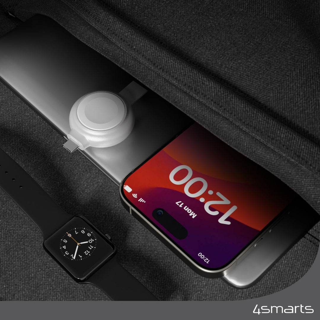 Ein 4smarts MFi Fast Charger für Apple Watch silber neben einer Powerbank und einem Smartphone in einer Tasche.